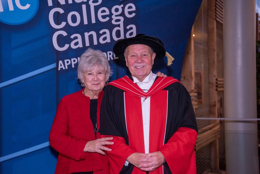 Saundra stands with Dan Patterson at the Welland Campus following his final convocation ceremony as president of NC in October 2019. they are pictured in front of a NC banner.