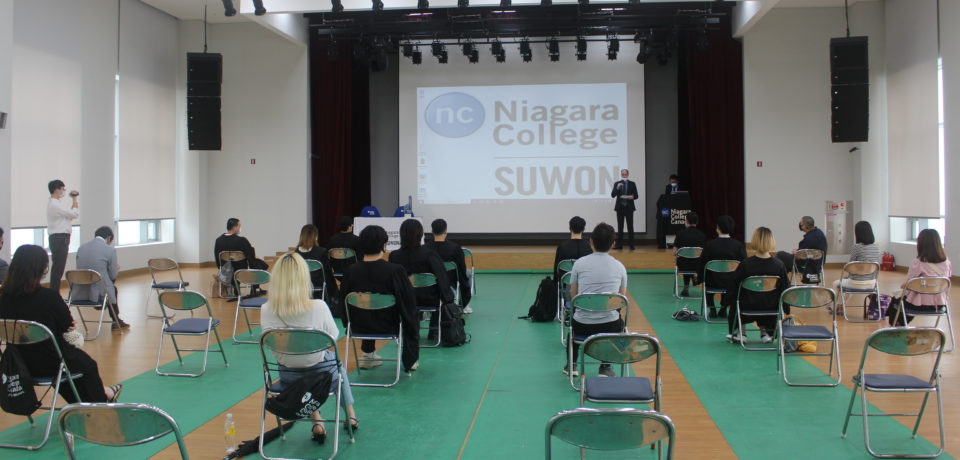 People sitting on folding chairs spaced apart, watching a presentation on an overhead