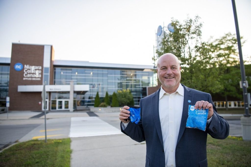 Sean Kennedy stands in front of the Welland Campus main entrance holding facemask kits