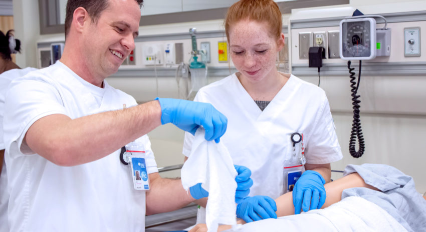 Student and teacher wearing scrubs and gloves