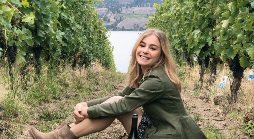 Host of Bottled in China Émilie Steckenborn (Wine Business Management, Class of 2011) is pictured in a scenic outdoor background with a bottle of wine.