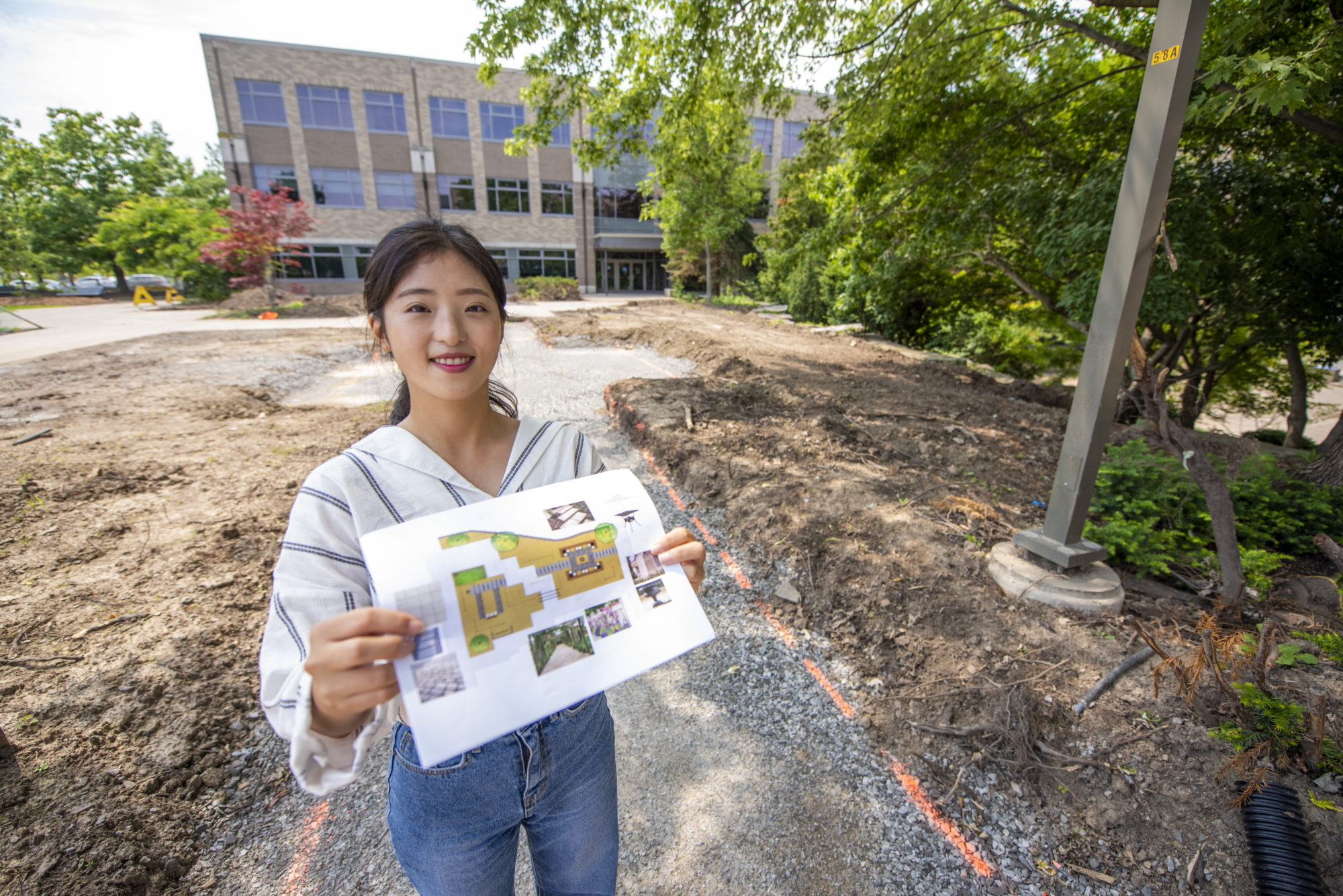 Student Alice Lee is holdiing up her design plans outside at the Daniel . Patterson Campus in Niagara-on-the-Lake where work is underway for the memorial garden.