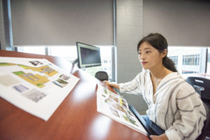 A student is pictured at a desgn table looking at papers containing designs for a garden. 