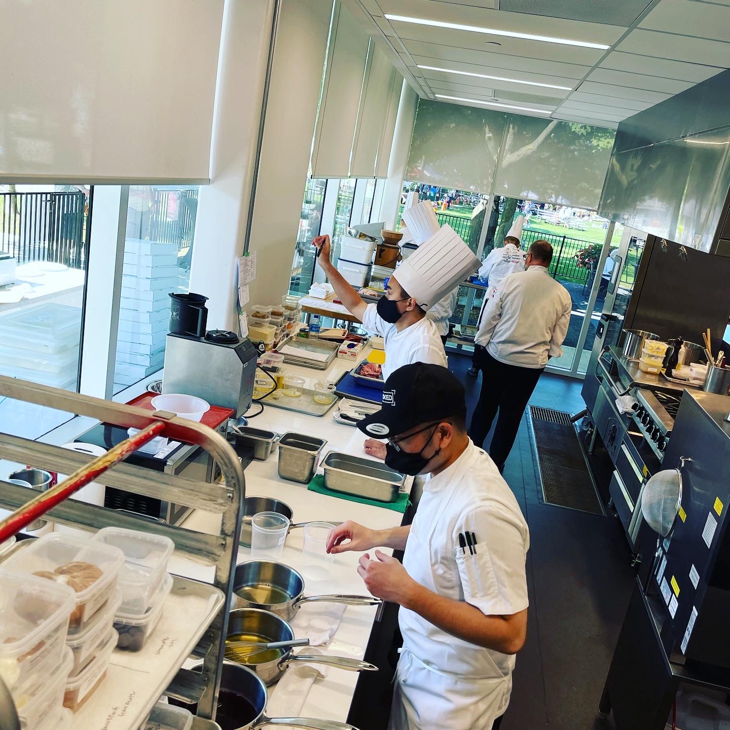 A team of chefs working in their whites are pictured in a kitchen, preparing food facing a window from inside the CFWI Aurora Armoury.