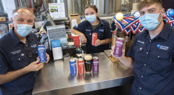 Staff and students in the brewery holding colourful cans of NC beer.