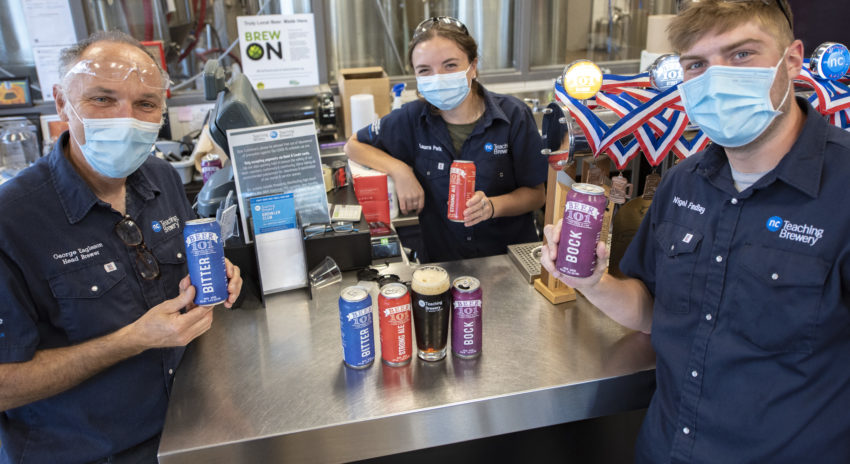 Staff and students in the brewery holding colourful cans of NC beer.