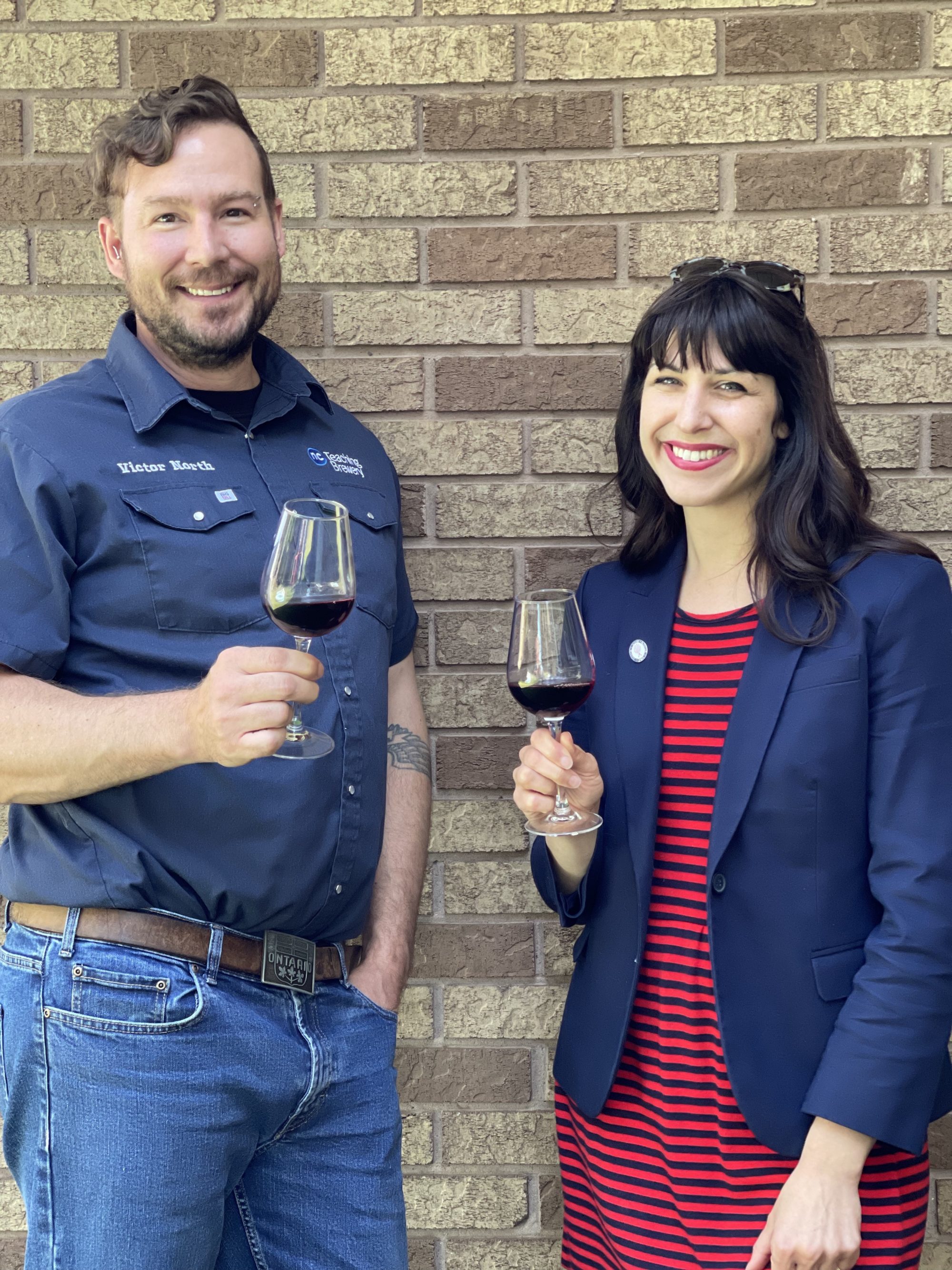 A man and woman stand outside with wine glasses.