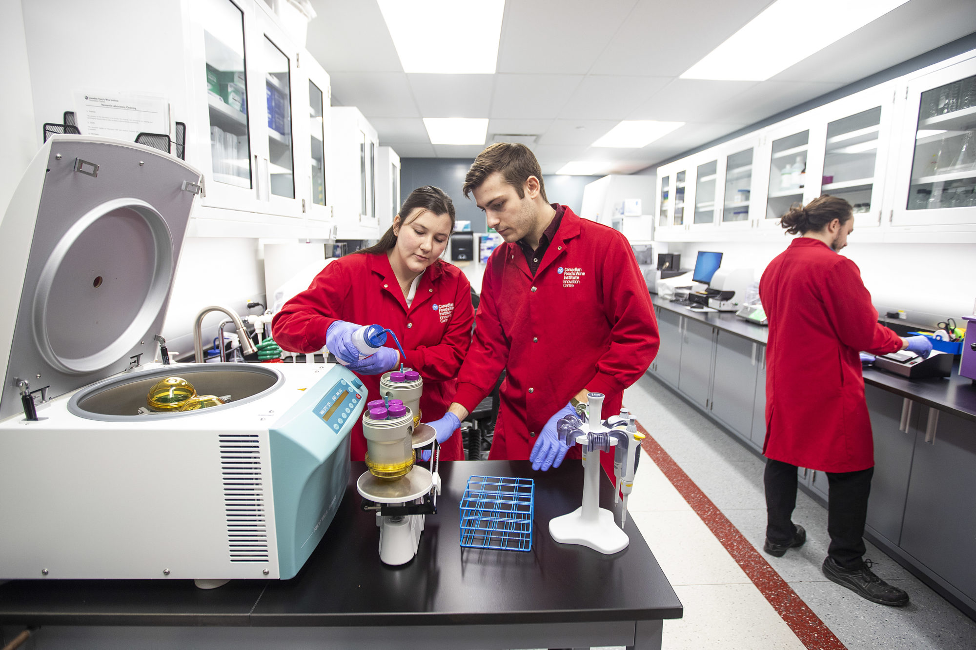 Two students wearing lab coats are working in a research lab.