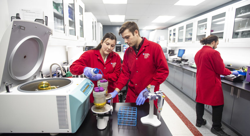 Two students wearing lab coats are working in a research lab.