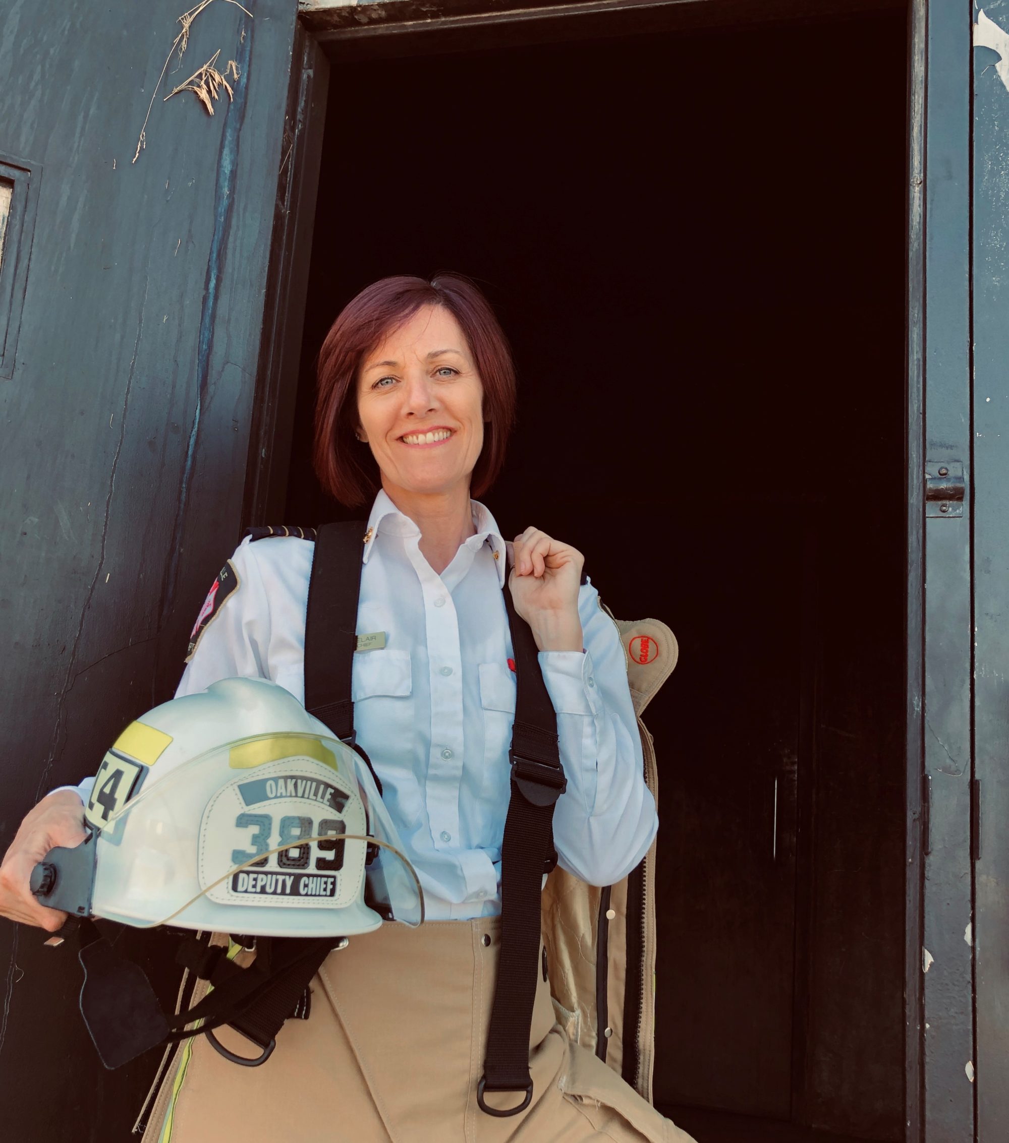 A woman in firefighter gear holding her hard hat