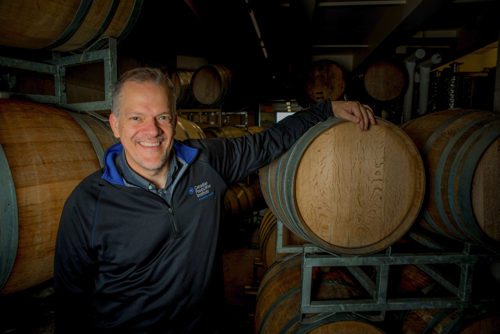 A man leans on a wine barrel and smiles.