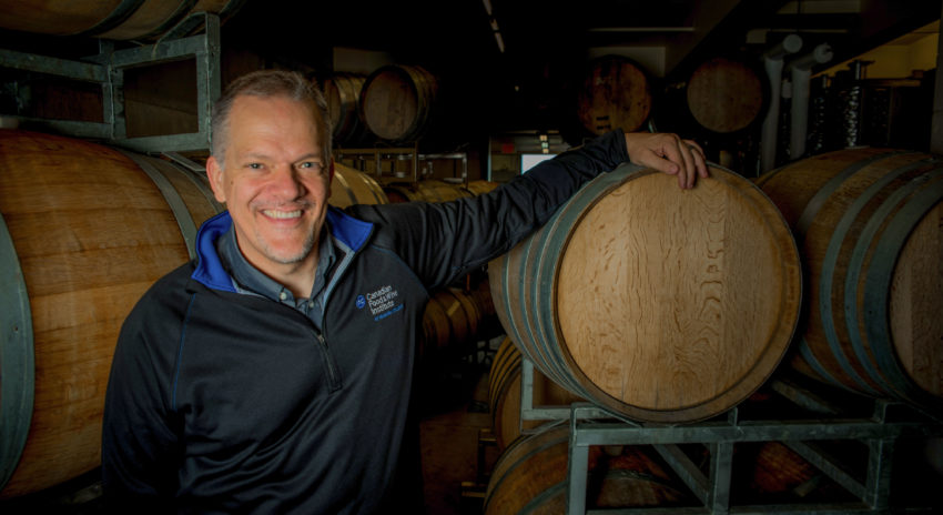 A man leans on a wine barrel and smiles.
