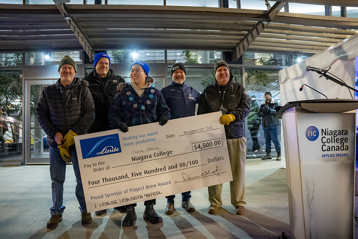 A group of people stand side by side holding a large cheque