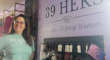 A woman wearing a green shirt stands alongside a wall bearing the words 39 Hers